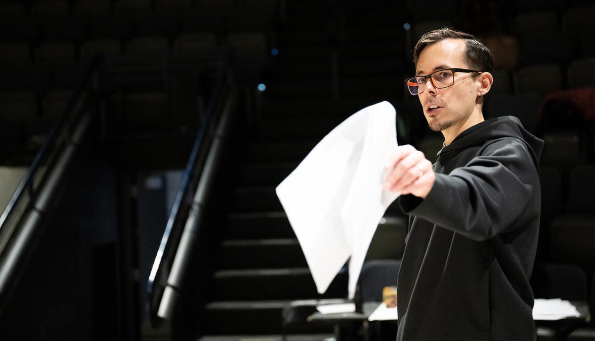 Héctor Alvarez holds a piece of paper and points on a dark stage